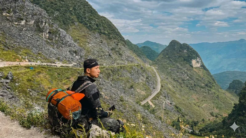 A traveler sitting above a winding mountain road on a 3-day Vietnam tour package, the Ha Giang Loop from Hanoi, Ha Giang, Vietnam